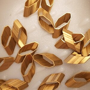 May include: A collection of gold-colored metal rings, some with a rounded shape and others with a more rectangular shape. The rings are arranged in a random pattern on a white surface.