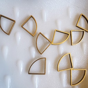 Könnte beinhalten: Eine Sammlung goldfarbener Metallformen, die jeweils einem Teilkreis oder einem Halbmond ähneln, verstreut auf einer weißen Oberfläche.