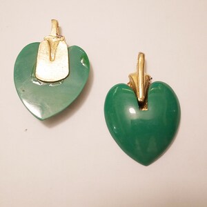 Puede incluir: Dos colgantes en forma de coraz&oacute;n verde con detalles dorados. Los colgantes tienen un acabado liso y brillante.