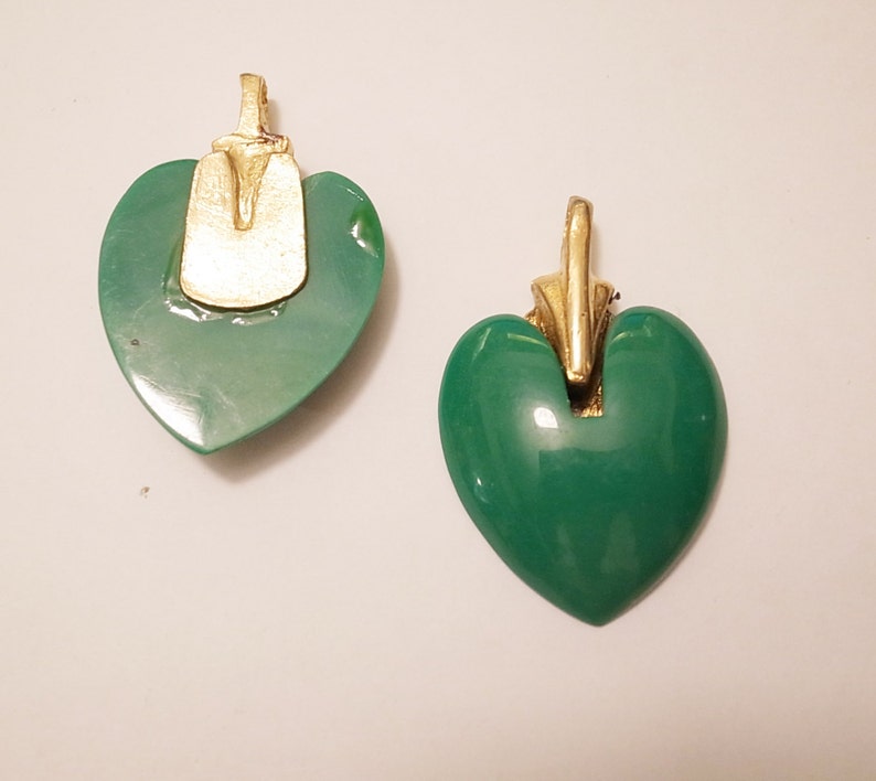 Puede incluir: Dos colgantes en forma de coraz&oacute;n verde con detalles dorados. Los colgantes tienen un acabado liso y brillante.