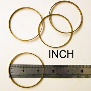 May include: Four brass rings of different sizes, measured with a ruler in inches. The rings are stacked on top of each other.