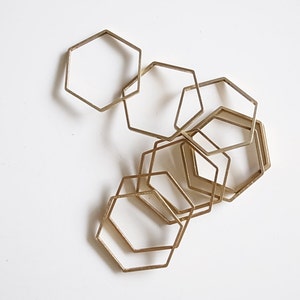 Puede incluir: Un conjunto de seis anillos hexagonales de metal dorado, superpuestos y superpuestos para crear un diseño geométrico.