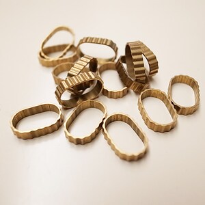 May include: A pile of small, gold-colored, metal rings with a textured, wavy edge. The rings are oval-shaped and appear to be made of brass.