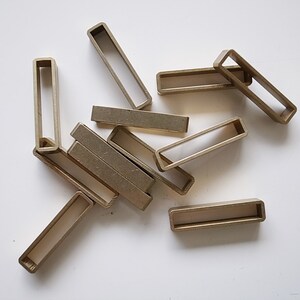 May include: A group of ten gold-colored metal rectangular buckles, some stacked on top of each other.