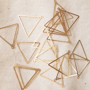 May include: A group of gold-coloured metal triangle shapes with rounded corners. The triangles are stacked on top of each other and are arranged in a random pattern.