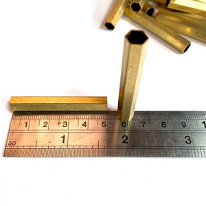 May include: A close-up of two brass hexagonal tubes measured against a ruler. The tubes are 1.6 cm and 3.8 cm long.