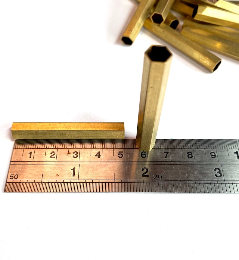 May include: A close-up of two brass hexagonal tubes measured against a ruler. The tubes are 1.6 cm and 3.8 cm long.