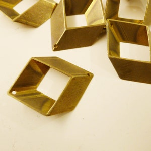 Op de afbeelding: Een groep van zes messing, vierkante, opengewerkte bedels met een geborstelde afwerking. De bedels hebben een gat aan de bovenkant om aan sieraden of andere knutselwerkjes te bevestigen.