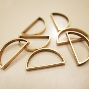 Pode incluir: Um conjunto de sete formas de semicírculo de metal dourado de tamanhos diferentes. As formas estão dispostas em um padrão aleatório sobre uma superfície branca.