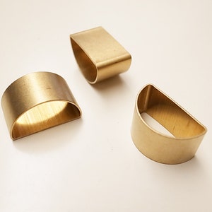 May include: Three gold-coloured metal rings, each shaped like a half-circle, are arranged on a white surface. The rings are different sizes.