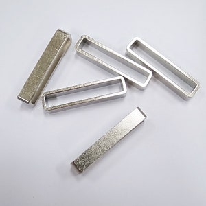 May include: Five silver metal rectangular rings with a textured surface. The rings are open on both ends and are approximately 1 inch long.