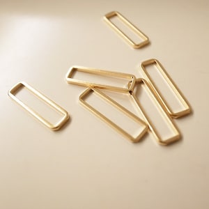 May include: Five gold-colored metal rectangular rings, some overlapping, on a white surface.