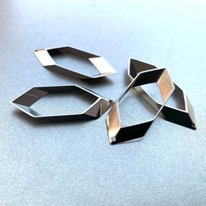 May include: Four geometric, open-frame metal components. Each component is a dark silver color with a contrasting light silver section. The components are in a scattered arrangement, suggesting they are jewelry findings or craft supplies.