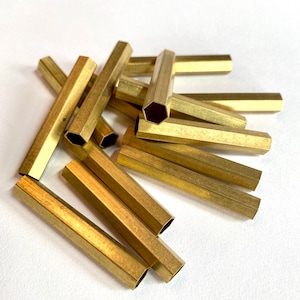 May include: A pile of gold-colored hexagonal brass tubes. The tubes are about 1 inch in diameter and 3 inches long.