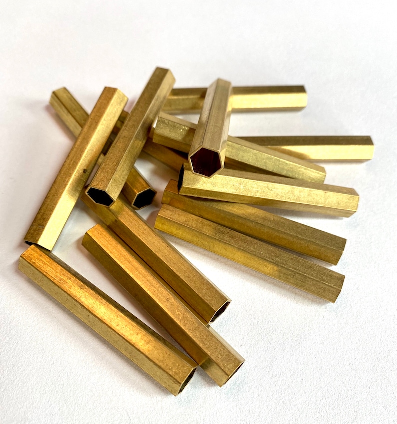 May include: A pile of gold-coloured hexagonal brass tubes. The tubes are approximately 2.5 cm in diameter and 7.5 cm long.