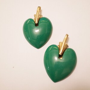 Puede incluir: Un par de pendientes colgantes en forma de coraz&oacute;n verde con detalles dorados. Los pendientes tienen un acabado brillante y lustroso.