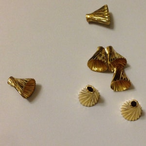 May include: A group of ten gold-colored metal cone-shaped beads. The beads have a fluted design and are arranged in a random pattern on a white surface.