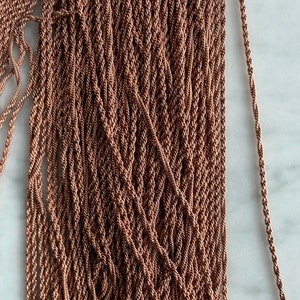 May include: Close-up of a pile of copper-colored twisted cord. The cord is tightly wound, creating a textured surface. The color is a warm, metallic tone, suggesting a jewelry or craft supply.