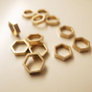 May include: A group of gold-toned metal hexagonal rings, some stacked on top of each other. The rings are smooth and shiny.