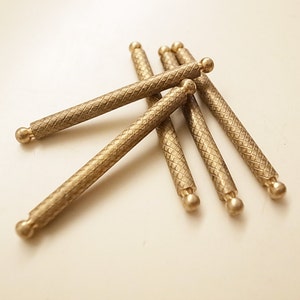 May include: Five gold-colored metal rods with a textured diamond pattern and rounded ends.