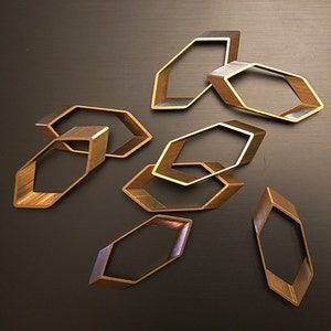 May include: A set of eight gold-toned metal geometric shapes, resembling hexagons, arranged in a random pattern on a dark brown surface.
