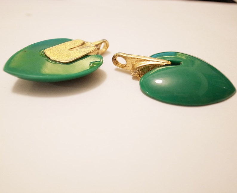 Puede incluir: Dos colgantes en forma de coraz&oacute;n verde con detalles dorados. Los colgantes tienen un acabado brillante y lustroso.