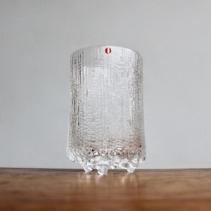 May include: A clear glass drinking glass with a textured surface and a wide base with three legs. The glass is empty.