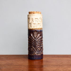 May include: A ceramic jar with a cork lid and a blue and brown glaze. The jar has a white band around the middle with the words "Parsley" and "Leaves" embossed on it. The jar has a decorative design of a stylized leaf on the bottom half.