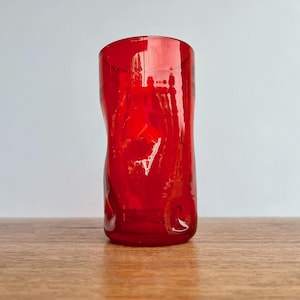 May include: A vibrant red glass tumbler with a unique, textured design. The glass has an irregular shape, adding to its artistic appeal. The tumbler is suitable for various beverages and adds a pop of color to any setting.