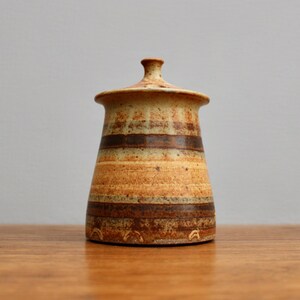 May include: A brown and cream ceramic jar with a lid. The jar has a striped pattern and is decorated with brown and cream glaze.
