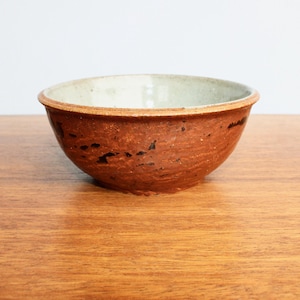May include: A small, brown ceramic bowl with a white interior. The bowl has a speckled brown glaze with black accents.