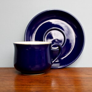 May include: A dark blue ceramic teacup and saucer set. The cup has a white rim and a rounded shape. The saucer is a simple round shape.