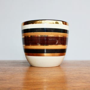 May include: A white ceramic planter with brown, black, and gold stripes.