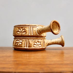 May include: A set of two brown and white ceramic soup bowls with floral designs and handles. The bowls are stacked on top of each other.