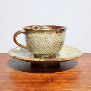 May include: A brown and cream ceramic teacup and saucer with a textured design. The cup has a handle and the saucer is round.