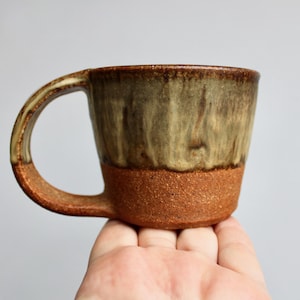 May include: A brown and green ceramic mug with a handle. The mug has a speckled glaze and a brown rim.