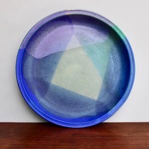 May include: A blue ceramic plate with a geometric design in shades of purple, green, and yellow.
