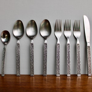May include: A set of silverware with a decorative pattern on the handles. The set includes a knife, fork, and spoons.