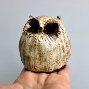 May include: A ceramic owl figurine with brown and white speckled glaze. The owl has large, round eyes and a rounded body.