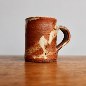 May include: A brown and white ceramic mug with a speckled glaze. The mug has a rounded handle.