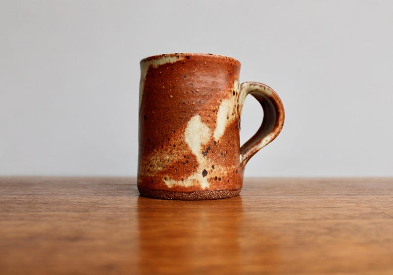 May include: A brown and white ceramic mug with a speckled glaze. The mug has a rounded handle.