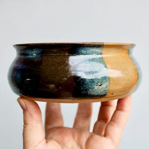 May include: A brown, blue, and tan ceramic bowl with a rounded shape. The bowl is glazed and has a glossy finish.