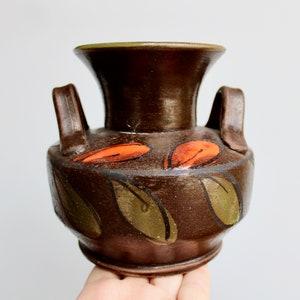 May include: A small brown ceramic vase with two handles and a painted design of green leaves and orange flowers.