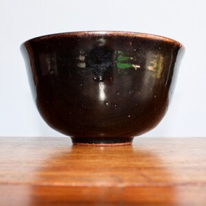 May include: A dark brown ceramic bowl with a slightly flared rim. The bowl has a glossy finish and sits on a small, circular base. The interior appears to be a darker shade of brown.