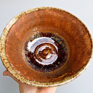 May include: A brown ceramic bowl with a light brown rim and a dark brown center. The bowl has a speckled glaze and a glossy finish.