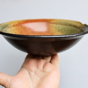 May include: A brown ceramic bowl with a speckled glaze. The bowl has a wide rim and a rounded bottom. The bowl is glazed in shades of brown, green, and orange.
