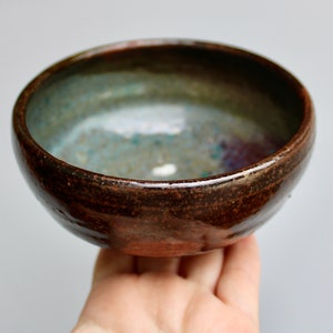 May include: A small, brown ceramic bowl with a speckled glaze. The inside of the bowl has a blue-green glaze with hints of purple.