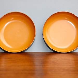 May include: Two orange ceramic bowls with a black rim. The bowls are empty and sitting on a wooden surface.