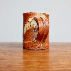 May include: A brown and white ceramic mug with a unique, textured handle. The mug has a rustic, handmade look.