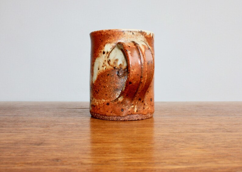 May include: A brown and white ceramic mug with a unique, textured handle. The mug has a rustic, handmade look.
